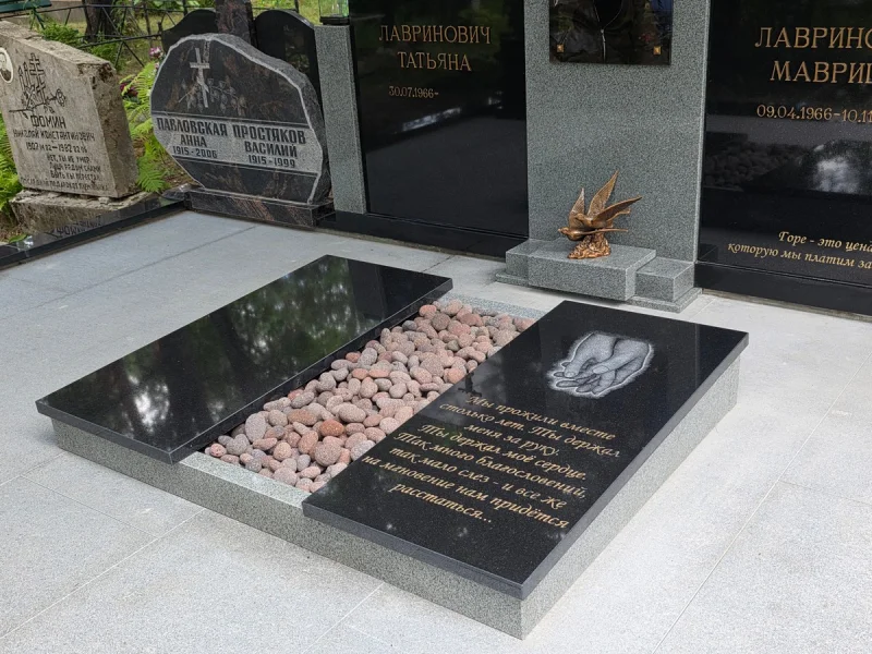 Slēgtās kapu plāksnes vienotā kompozīcijā ar gravējumu un dekoratīvajiem krāsainajiem oļiem.